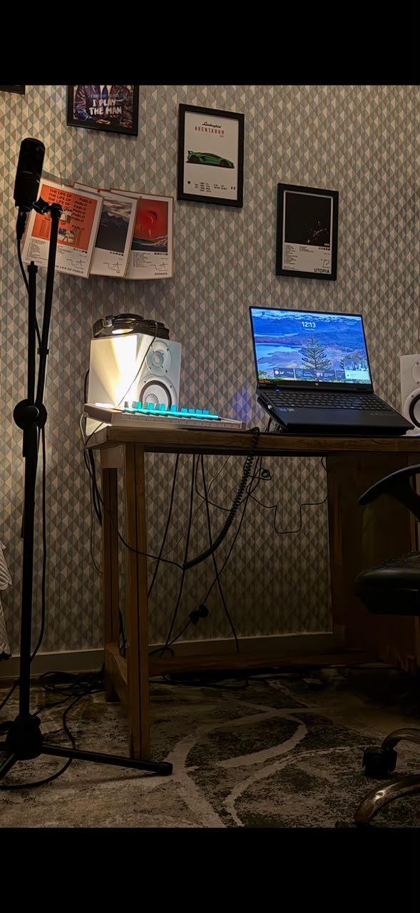 Chirag's home studio — condenser mic on a boom stand, laptop with studio monitors, mechanical keyboard, and framed music posters on a diamond-patterned wall.
